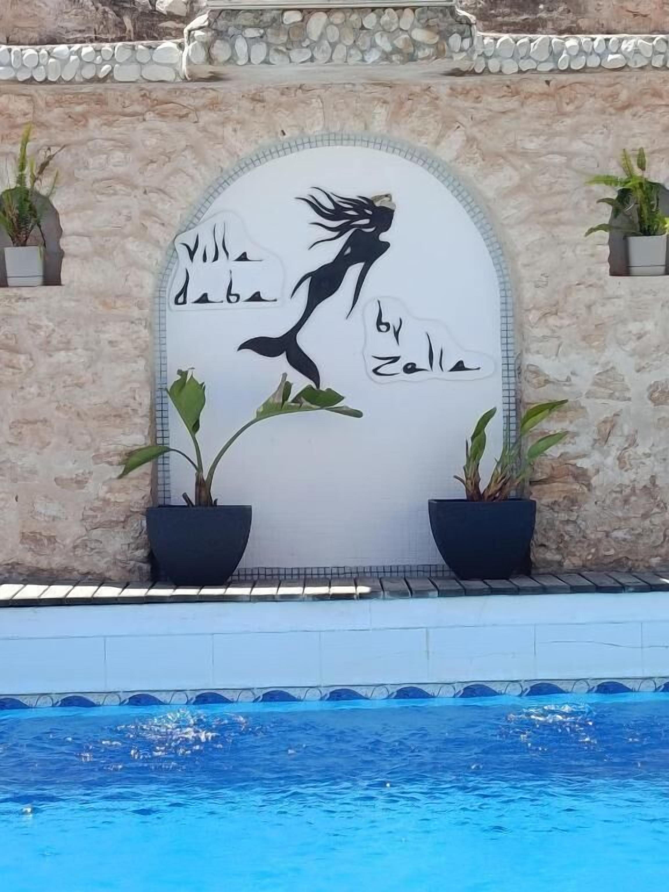 Area piscina con un murale di una sirena e piante in vaso.