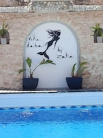 Un área de piscina con un mural de una sirena y plantas en macetas.