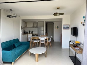 Ein gemütlicher, kompakter Wohnbereich mit Sofa, Esstisch, Stühlen, Fernseher und Küchenzeile.