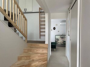Ein Flur mit einer Holztreppe, einem grünen Sessel und einem an der Wand befestigten Kunstwerk.