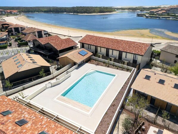 Ein Pool, umgeben von Gebäuden mit Ziegeldächern, mit Blick auf einen Strand und das Wasser.