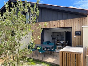Ein modernes Gebäude mit Holzfassade, einer Terrasse mit Tisch und Stühlen sowie einem Schild mit der Aufschrift 'Maison Bourbon'.