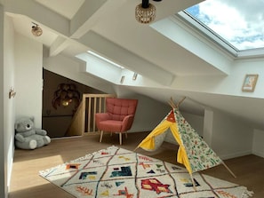 Ein Zimmer mit einem Oberlicht, einem roten Stuhl, einem Teddybären, einem farbenfrohen Teppich und einem Tipizelt.
