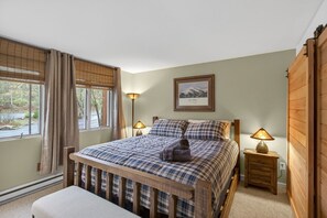 A bedroom with a bed, bedside lamps, a framed picture on the wall, and a window with curtains.