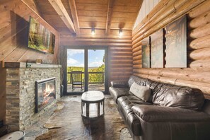A log cabin interior with a stone fireplace, leather sofa, and wooden walls. - Whiskey Den-Serene&Natural Cabin-7 mi to Downtown (Eureka Springs)