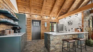 A log cabin-style kitchen with a stone island, bar stools, and a stone wall. - Pine Haven-Serene & Natural Cabin-7 mi to Downtown (Eureka Springs)