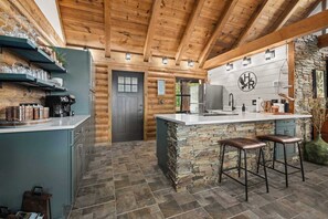 A log cabin-style kitchen with a stone island, bar stools, and a stone wall. - Pine Haven-Serene & Natural Cabin-7 mi to Downtown (Eureka Springs)