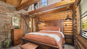 A log cabin bedroom with a bed, wooden headboard, stone wall, and a window with blinds. - Pine Haven-Serene & Natural Cabin-7 mi to Downtown (Eureka Springs)