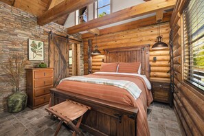 A log cabin bedroom with a bed, wooden headboard, stone wall, and a window with blinds. - Pine Haven-Serene & Natural Cabin-7 mi to Downtown (Eureka Springs)