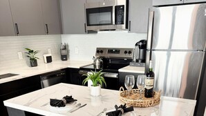 A modern kitchen with a marble island, stainless steel appliances, and blue bar stools. - Cozy Chic 1 Bdrm King Suite - mins to NYC, MetLife (Belleville)
