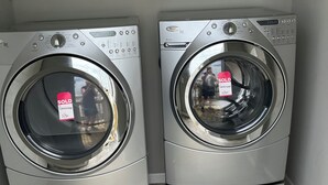 Zwei Waschmaschinen mit Frontlader in einem Waschraum mit einem Metallregal darüber.
