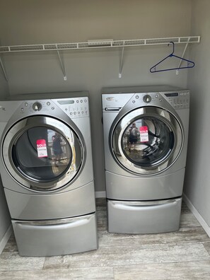 Deux machines à laver à chargement frontal se trouvent dans une buanderie, avec une étagère en métal au-dessus.