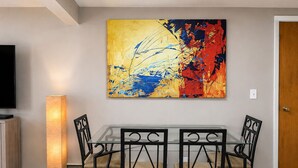 Un coin repas avec une table en verre et quatre chaises, un lampadaire et un grand tableau abstrait accroché au mur.