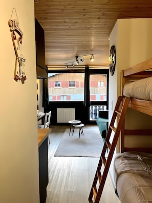 Een kamer met een stapelbed, een kleine tafel, een stoel, een 'Welcome' bord en uitzicht op een gebouw.