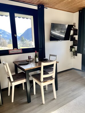 Un comedor con una mesa, sillas, una botella de vino y un televisor en la pared.