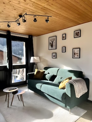 Een woonkamer met een groene bank, een lamp, een salontafel en een raam met gordijnen.