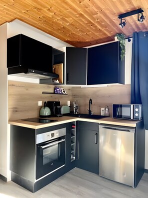 Una cocina compacta con electrodomésticos integrados, techo de madera y salpicadero oscuro.