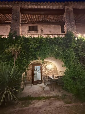 Une terrasse extérieure avec une table et des chaises, une porte donnant sur une cuisine et un mur en pierre.