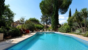 Piscina retangular com borda azulejada, rodeada por vegetação e algumas cadeiras de exterior.