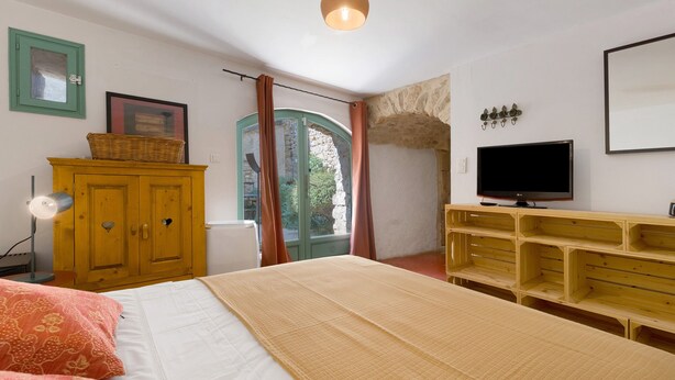 Quarto com cama, cômoda de madeira, televisão e janela com cortinas.