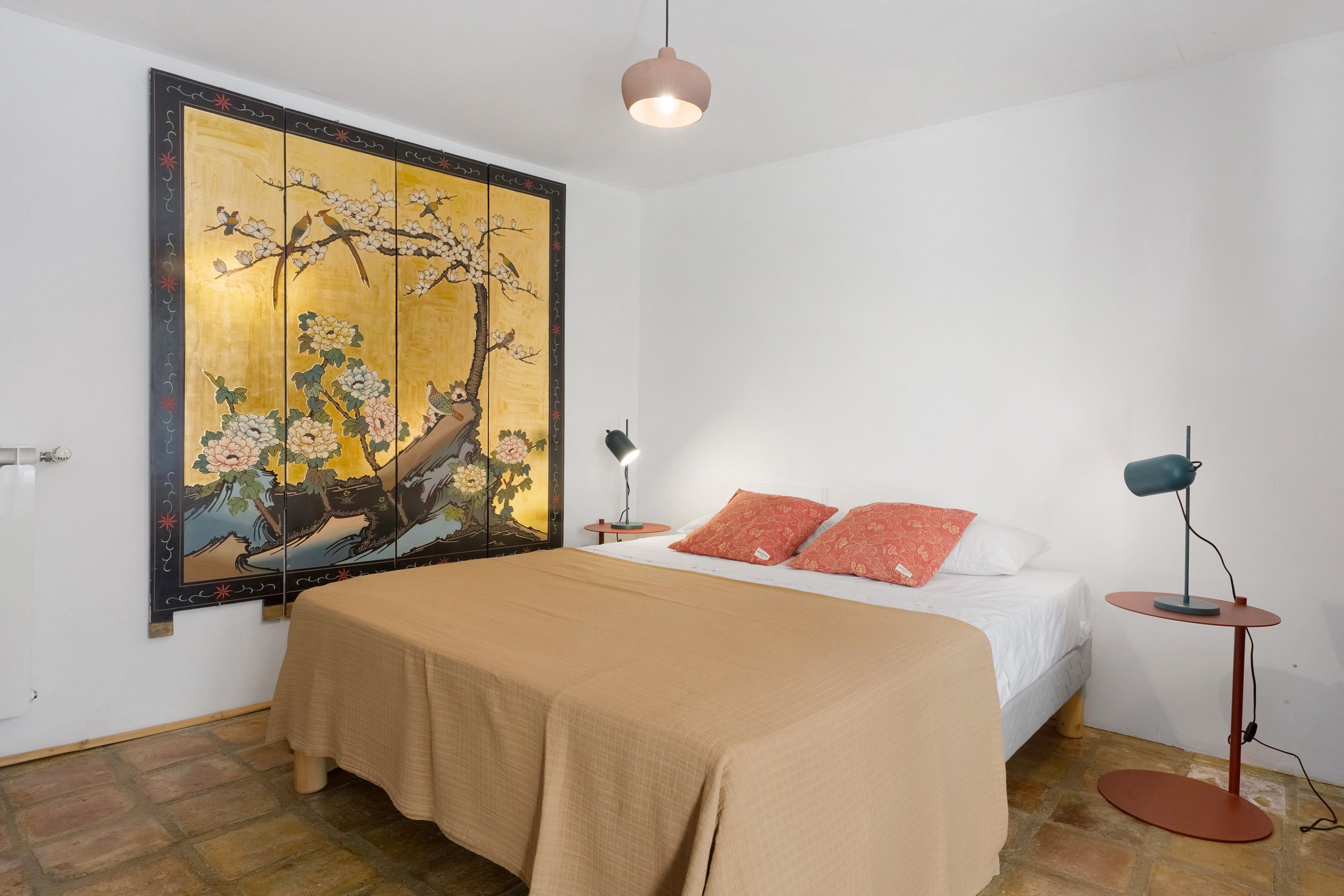 Une chambre à coucher avec un lit, une table de chevet, une lampe sur pied et un grand tableau accroché au mur.