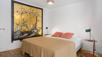 Un dormitorio con cama, mesita de noche, lámpara de pie y un cuadro grande en la pared.