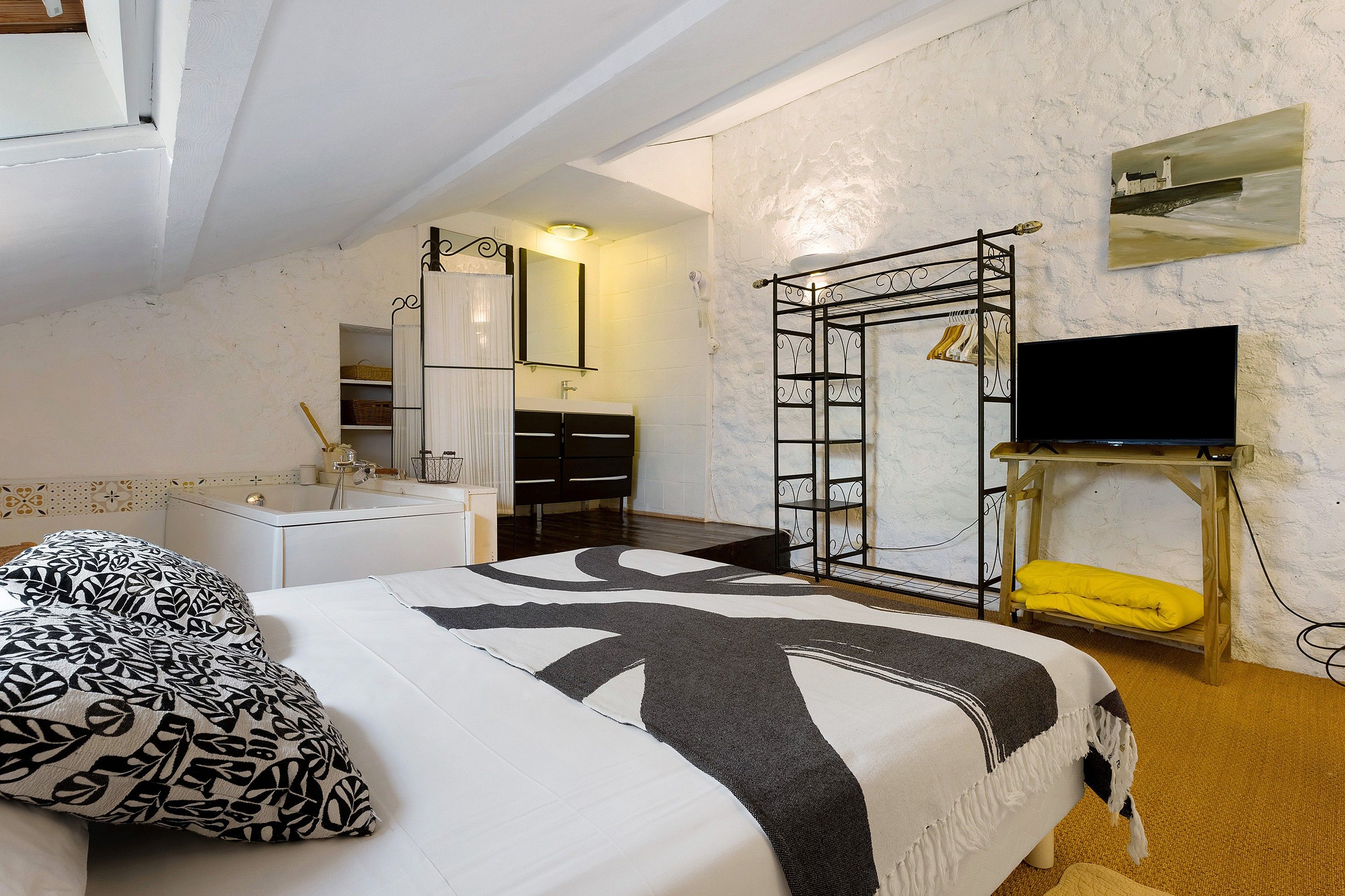 Ein Schlafzimmer mit einem Bett, einem Nachttisch, einem Spiegel, einem Kleiderschrank, einem Fernseher und einem Kleiderständer.