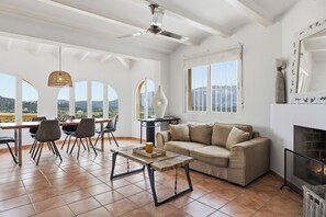 Un salon spacieux avec un haut plafond, de grandes fenêtres, une cheminée et un coin repas comprenant des chaises et une table.