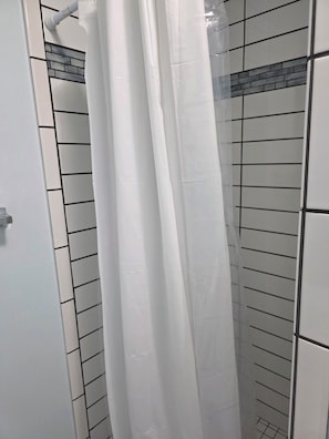 A shower area with white tiled walls and a white shower curtain.