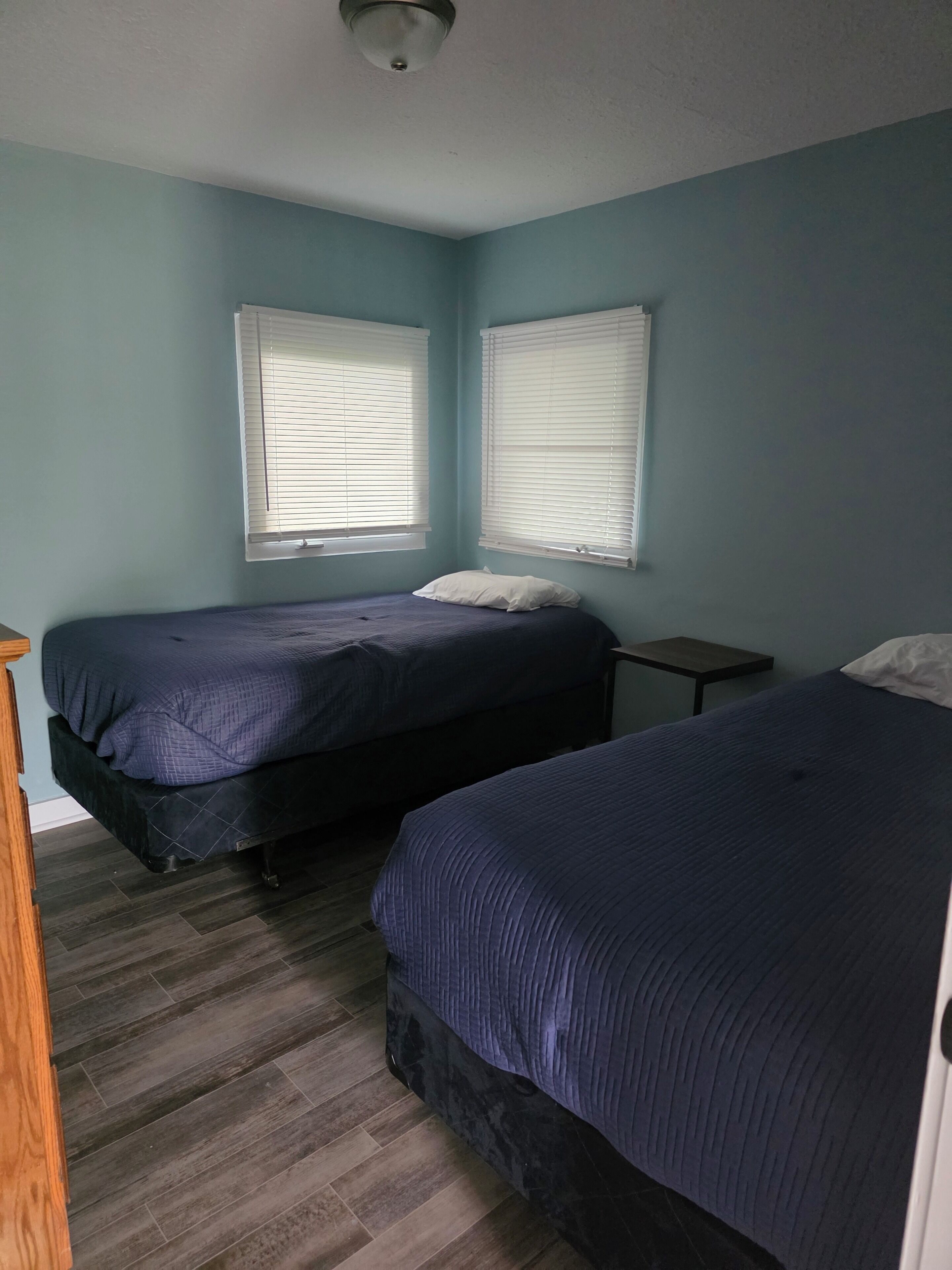 Quarto com duas camas, uma mesinha de cabeceira de madeira e uma pequena mesa.