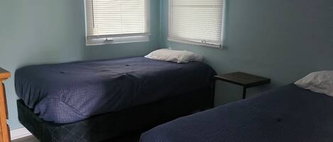 Quarto com duas camas, uma mesinha de cabeceira de madeira e uma pequena mesa.