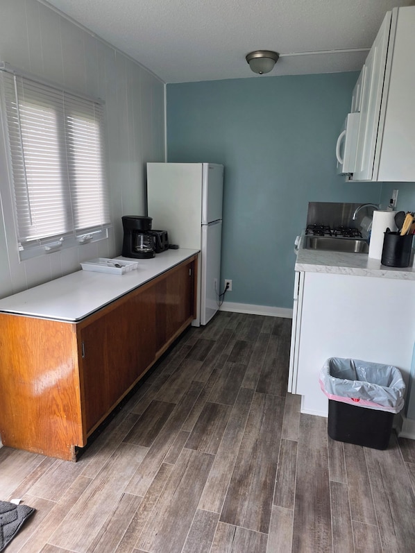 A compact kitchen with a white refrigerator, wooden cabinets, a gas stove, and a trash bin.