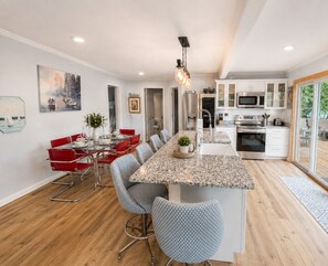 Una cocina moderna con una isla central, electrodomésticos de acero inoxidable y un comedor con sillas rojas.