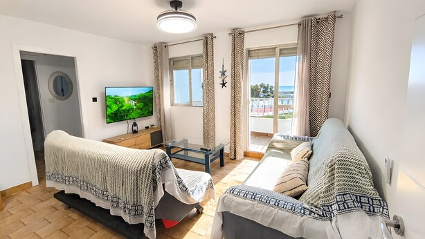 Ein Wohnzimmer mit einer Couch, einem Couchtisch, einem Fernseher und Blick ins Freie.