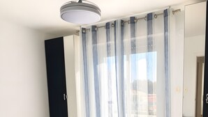Ein Schlafzimmer mit Bett, Deckenventilator, Fenster mit Vorhängen und Blick nach draußen.