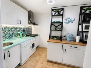 Een kleine keuken met een wasmachine, een spoelbak, een magnetron en een plank met keukengerei.