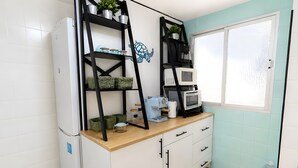 Eine Küche mit weißen Schränken, einem weißen Kühlschrank, einer Holz Arbeitsplatte, einem schwarzen Metallregal mit Pflanzen, einer Mikrowelle und einem Fenster mit Blick.