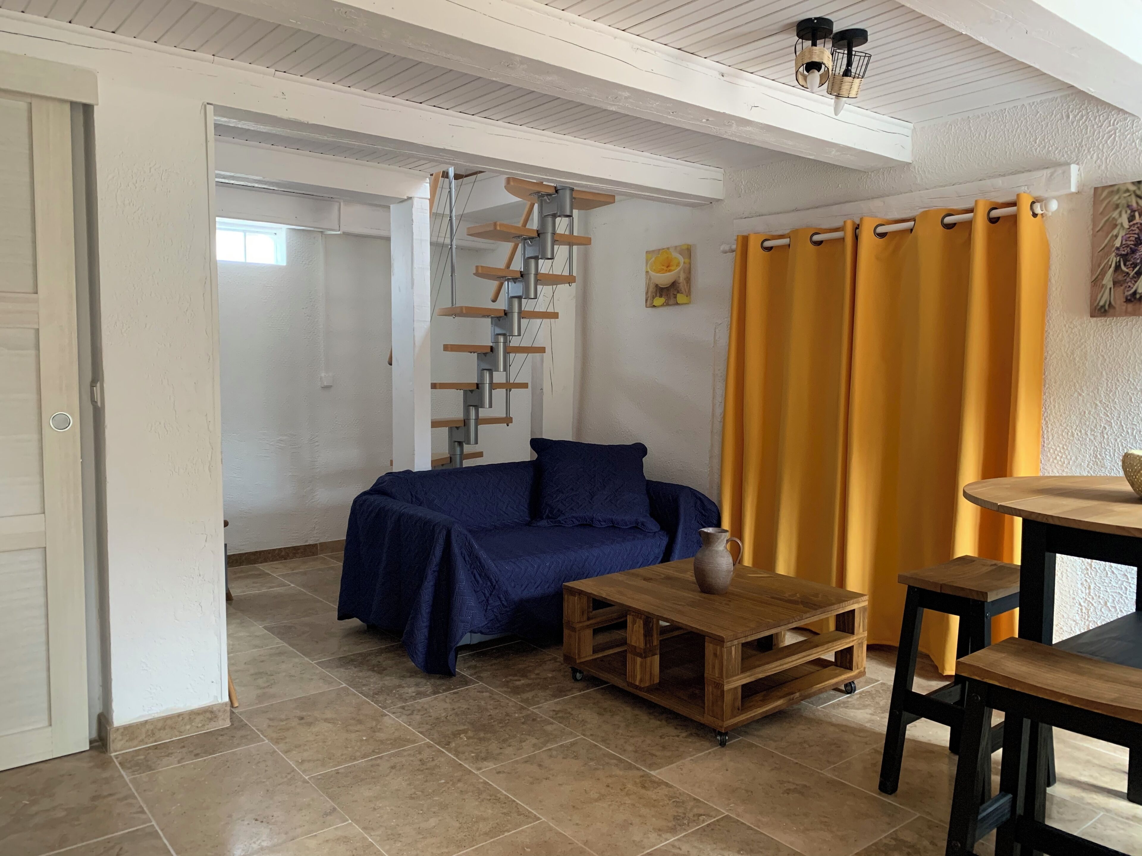 Ein Zimmer mit einem blauen Sofa, einem Holztisch mit einer Vase, gelben Vorhängen und einer Treppe.