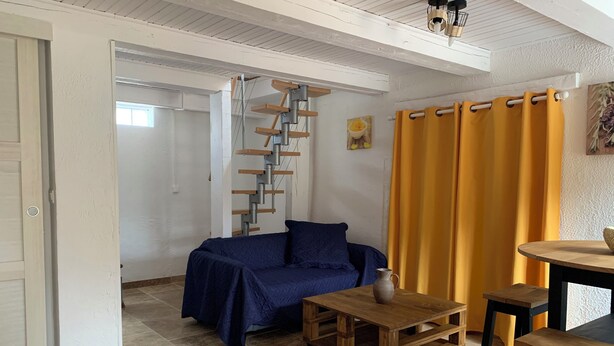 Una habitación con un sofá azul, una mesa de centro de madera con un jarrón, cortinas amarillas y una escalera.