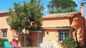 Una casa con techo de tejas, un patio con mesa y sillas, y un árbol en el jardín.