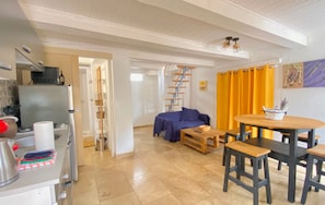 Ett kompakt bostadsutrymme med ett köksområde, ett matbord med stolar, en soffa och en stege som står lutad mot väggen.