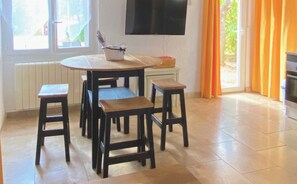 Eine Küche mit einem runden Tisch, vier Barhocker, einem Fernseher über dem Tisch und einem Fenster mit Vorhängen.