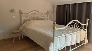 Una cama individual con estructura metálica blanca, una mesita de noche pequeña y una lámpara fijada a la pared.