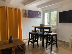 Ein Essbereich mit einem runden Tisch, vier Stühlen, einem kleinen Tisch mit einer Karaffe und einem an der Wand befestigten Fernseher.
