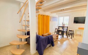 Eine mehrgeschossige Holztreppe, ein Essbereich mit Tisch und Stühlen sowie eine gemütliche Sitzecke mit einer Decke.