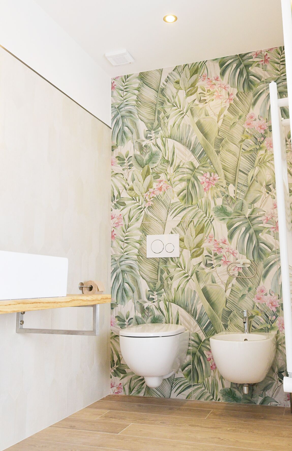 A bathroom with a floral wallpaper, two sinks, a wooden shelf, and a white towel rack.