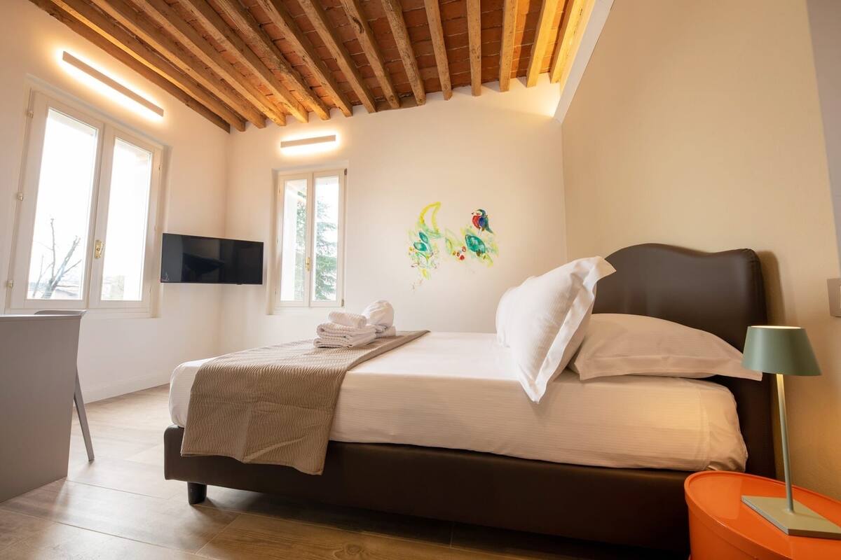 Un dormitorio con cama, televisor montado en la pared y ventana.