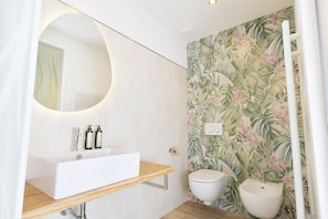A bathroom with a white sink, two toilets, a mirror, and a wall with a tropical leaf pattern. - Il Drago di San Giorgio (San Giorgio di Piano)