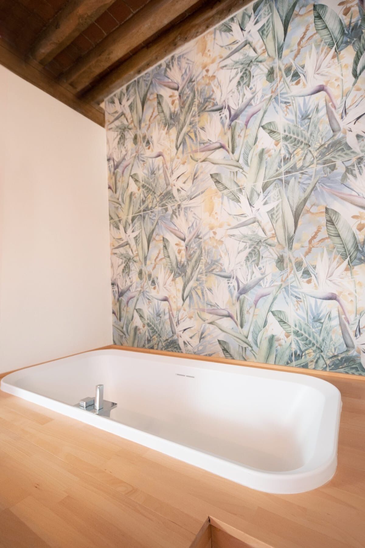 A modern bathroom with a freestanding bathtub, wooden vanity, and a tropical-themed wallpaper.