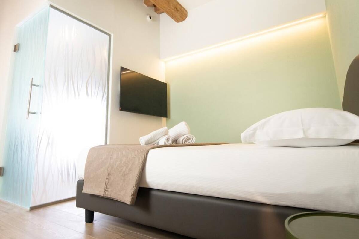 Un dormitorio moderno con una cama, un televisor montado en la pared y una viga de techo de madera.